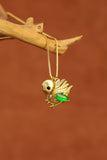 Lucky Songbird pendant featuring natural Burmese green jade, displayed on a rustic wooden branch. Handcrafted gold bird necklace inspired by nature, hope, and freedom.